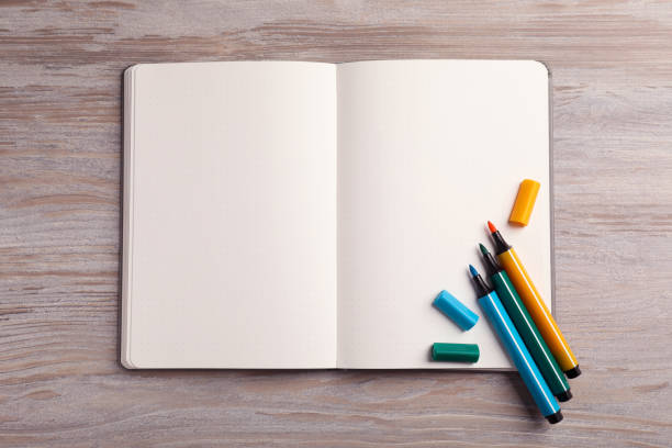 istock Open notebook and colorful markers on light wooden table, top view 1935589776