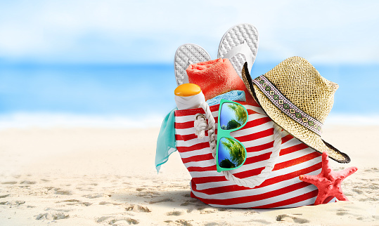 Summer beach bag and accessories on sandy beach and sea.