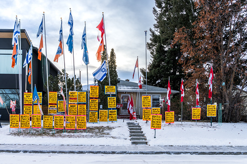 Edmonton, Canada, December 10, 2023: City of Edmonto residential area house front yard with   political agenda posters  and multiple flags on dark sky clouds background in winter season