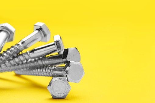 Many self-tapping screws on yellow background, closeup. Space for text