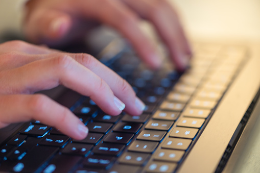 Extreme Close up of a woman’s hands typing on a laptop computer keyboard.