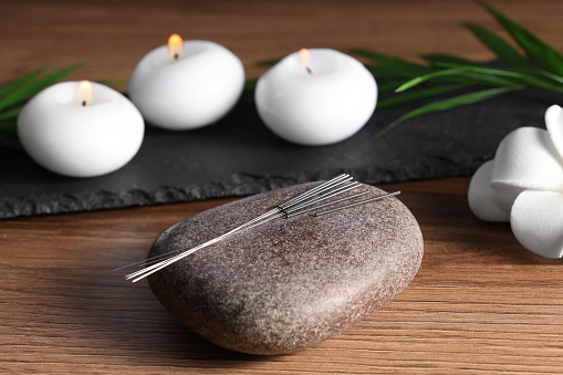 Stone with acupuncture needles and burning candles on wooden table