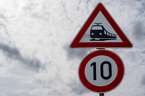 Railroad sign and 10 kilometers per hour sign with cloudy sky in background