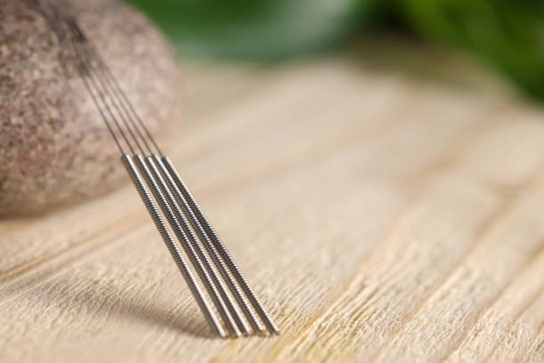 Acupuncture needles and spa stone on wooden table, closeup. Space for text