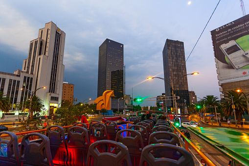 Mexico city, Mexico  - March 15,2022: Touristic hop on-hop off bus in night city Mexico City,  near Torre del Caballito Skyscraper and Caballito sculpture