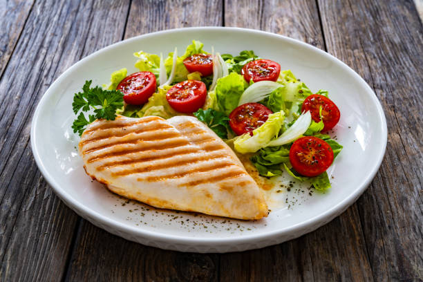 istock Grilled chicken breast with tomatoes and lettuce on wooden table 1935638360