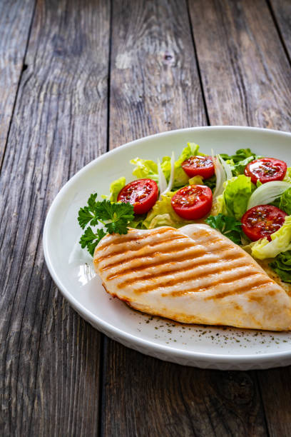 istock Grilled chicken breast with tomatoes and lettuce on wooden table 1935638884