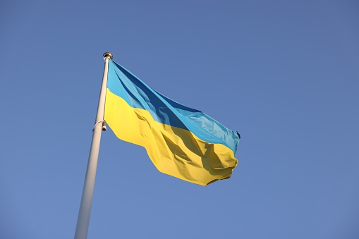 Flag of Ukraine fluttering against blue sky, low angle view