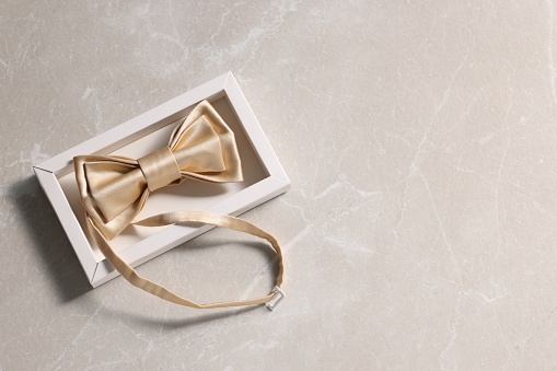 Stylish pale yellow bow tie on beige marble background, top view