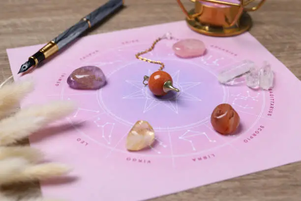 Astrology prediction. Zodiac wheel, gemstones and pendulum on wooden table, closeup