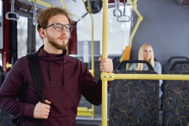 istock Man in glasses with backpack looking seriously at window in moving bus. 1935648594