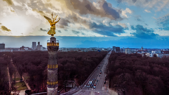 Awe sunset Drone point of view  on Victory column  with Golden statue on top, 67m (1864)  and Bundesstrasse 2 and Bundesstrasse 5   in  Tiergarten of Berlin  (in direction on West). Cars are waiting at the intersection on Grosser Stein