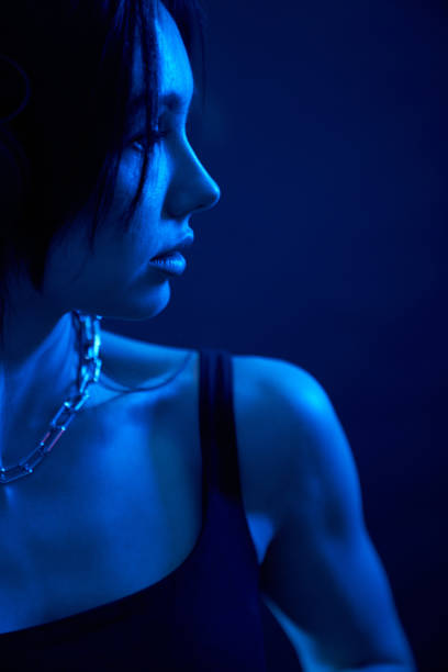 istock Tranquil young woman in top looking away in studio with dark blue illumination. 1935655981