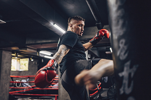 Fit male kickboxer training with punching bag in gym alone.