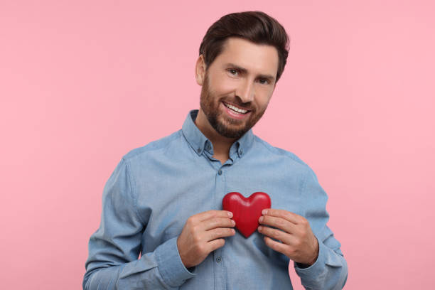 istock Happy man holding red heart on pink background 1935705447