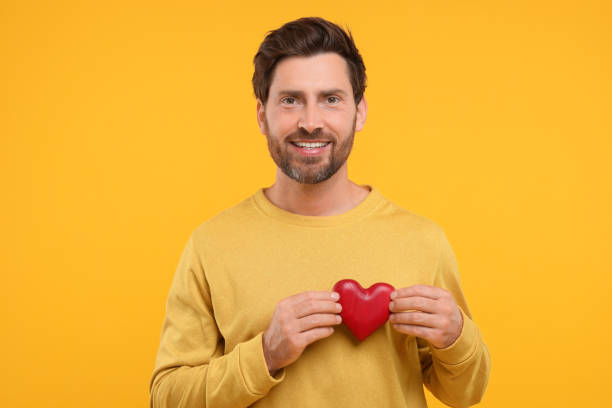 istock Happy man holding red heart on orange background 1935705450