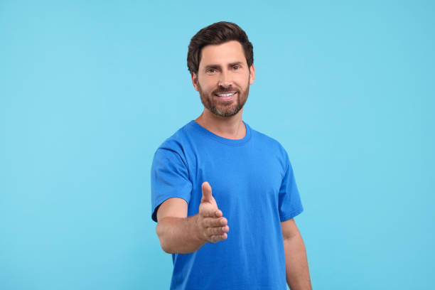 istock Happy man welcoming and offering handshake on light blue background 1935705957
