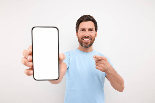 istock Handsome man showing smartphone in hand and pointing at it on white background 1935705962