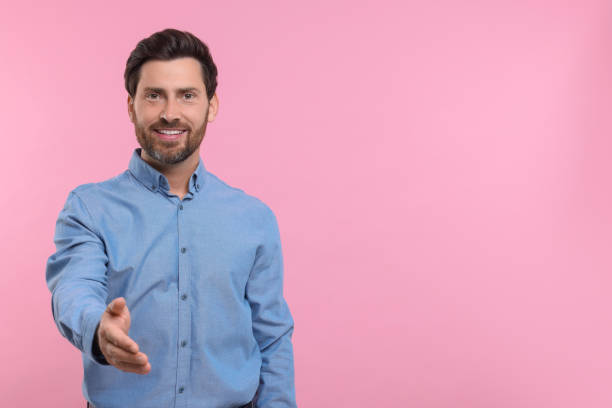 istock Happy man welcoming and offering handshake on pink background. Space for text 1935705973