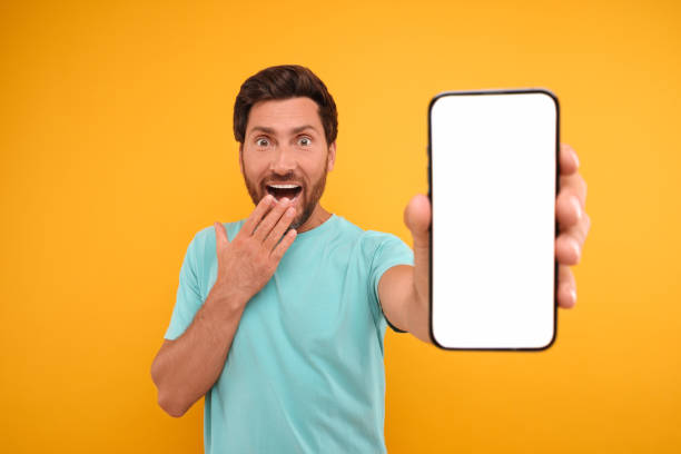 istock Surprised man showing smartphone in hand on yellow background 1935705977