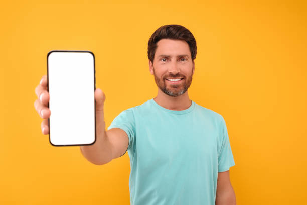 istock Handsome man showing smartphone in hand on yellow background 1935706482