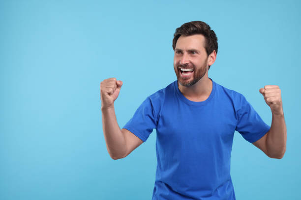 istock Emotional sports fan celebrating on light blue background, space for text 1935710155