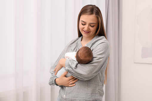 Happy mother with her cute newborn baby indoors. Space for text