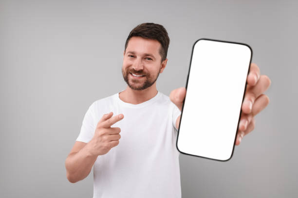 istock Handsome man showing smartphone in hand and pointing at it on light grey background 1935744949