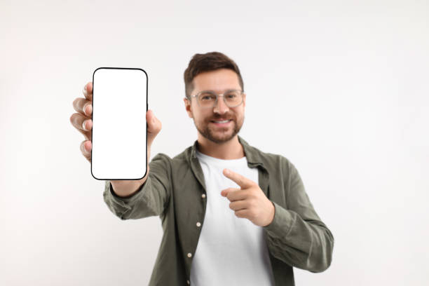 istock Handsome man showing smartphone in hand and pointing at it on white background, selective focus. Mockup for design 1935747047