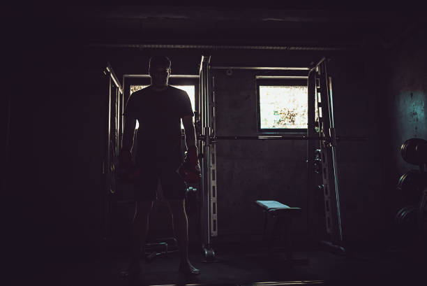 One man only / one person / rear view / waist up of 20-29 years old handsome people brown hair / short hair caucasian male / young men athlete / sportsperson exercising / standing in front of white background wearing sports clothing / running shorts / shorts / sports shoe who is of muscular build / serious / confidence / concentration and showing hand raised and being active with barbell / weightlifting / weight training / weights / cross training / body building / heavy