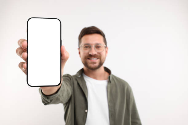 istock Handsome man showing smartphone in hand on white background, selective focus. Mockup for design 1935748117