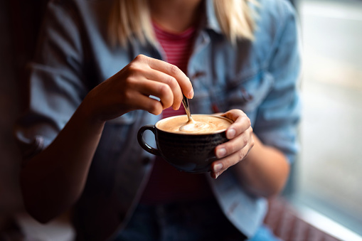 Close up shot of an anonymous woman holding a cup of coffee and stirring it with a teaspoon.