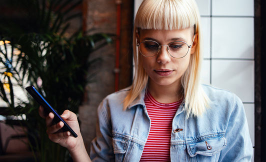 Close up of a beautiful young creative woman with blonde hair holding a mobile phone, listening to a voice message and looking down.
