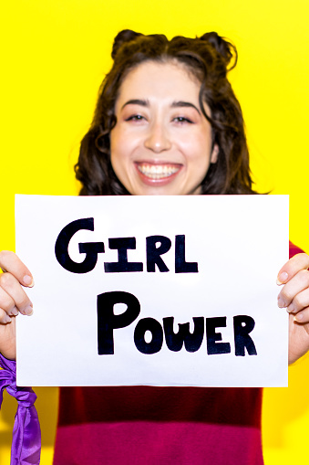 Young latina woman holding a sign with the text GIRL POWER on yellow background. Concept of the struggle for equality and women's rights.