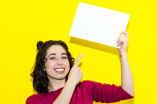 young smiling latin woman pointing with finger on white board isolated on yellow background