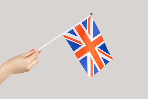 Closeup of woman hand showing british flag, traveling to Britain, immigration. Indoor studio shot isolated on gray background.
