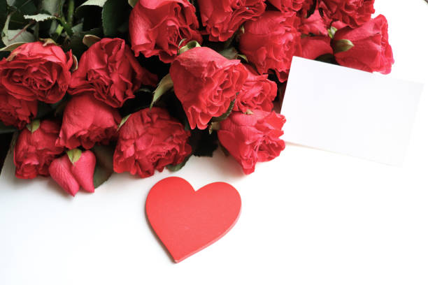 A heart shape cut out of pink paper that exposes a bed of red roses.