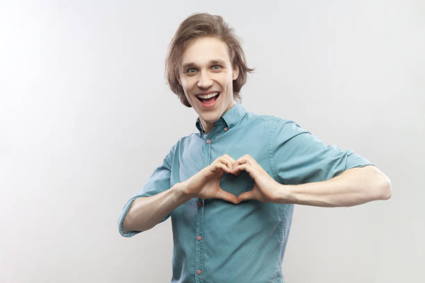 istock Smiling cheerful man showing heart shape with fingers, expressing love, affection, looking at camera 1935873656