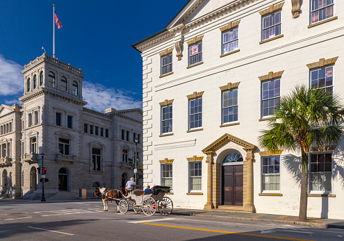 Charleston, South Carolina, USA - September 10, 2023: A couple enjoy a horse carriage tour down Meeting Street as they pass in front of the County of Charleston Historic Courthouse.