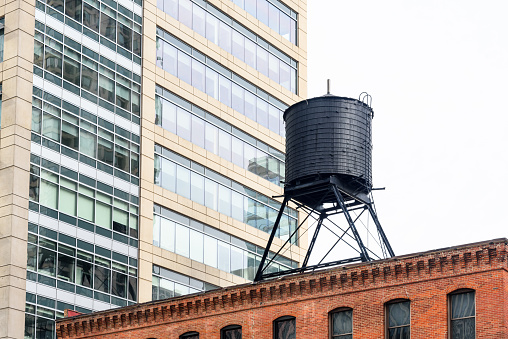 Low angle view of a traditional water tank on the roof of an old brick building in a downtown district on a cloudy spring day. a modern high rise office building is in background. Chicago, IL, USA.