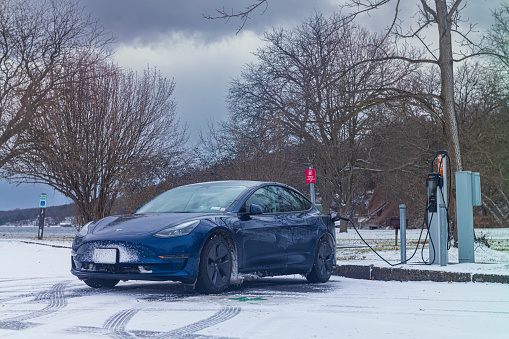 Trumansburg, NY, USA - Jan 14, 2023:  A Tesla Model 3 charges at a Level 2, ChargePoint station at Taughannock Falls State Park during a cold January winter. day.
