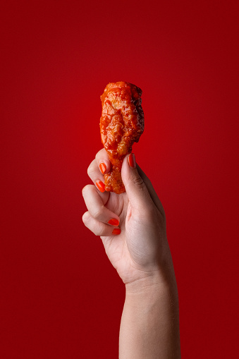 A woman's hands are seen holding a a fried chicken drumstick against a vibrant red background.