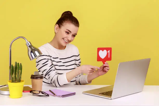 Photo of Woman sitting at workplace, asking to rate her posts showing likes counter template to laptop screen