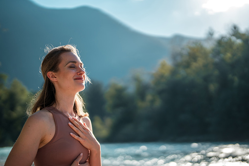 A Caucasian female enjoys breathing exercises and meditation on a yoga mat, soaking up the sun along the tranquil Soča river.