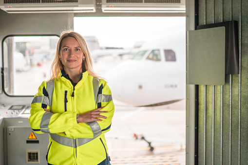 Confident mid adult Caucasian female engineer working at the airport. She is looking at the camera with her arms crossed.