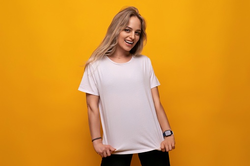 joyful woman showing on blank mockup white t-shirt on yellow background.