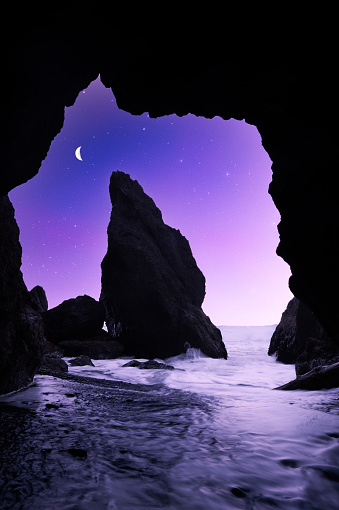 A fine art landscape photography image of a prominent sea stack at Ruby Beach shot in a sea cave with a twilight sky illuminating the crashing waves.