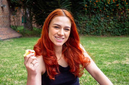 Beautiful young woman eating apple outside