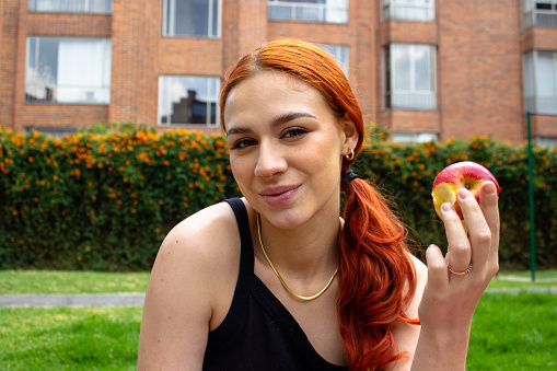 Beautiful young woman eating apple outside