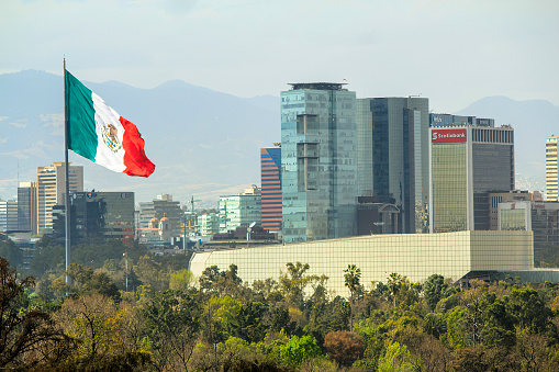 Mexico City, Mexico. Jan 14, 2024. The Mexican flag gracefully sways in the wind, set against the backdrop of modern corporate buildings and the iconic National Auditorium in downtown Mexico City.